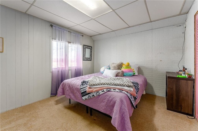 bedroom with a drop ceiling, carpet, and brick wall