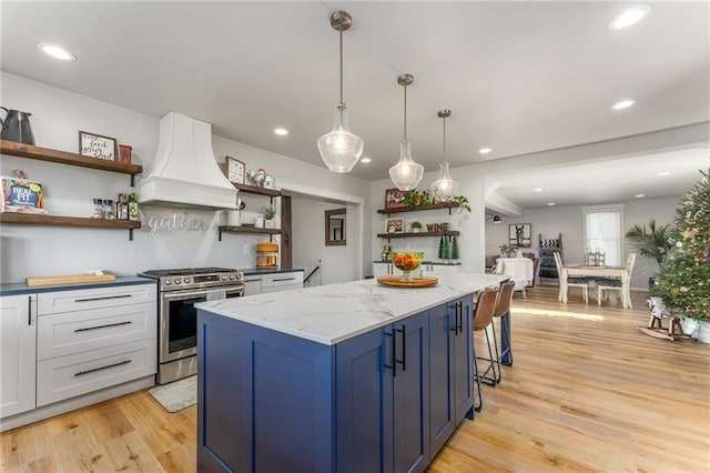 kitchen with a kitchen island, premium range hood, stainless steel range with gas stovetop, light wood-type flooring, and open shelves