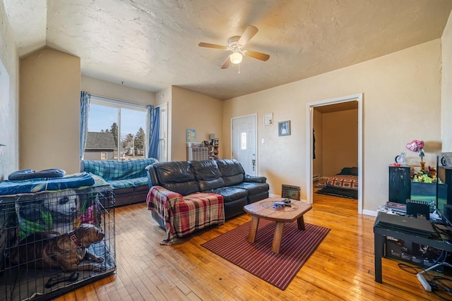 living area featuring baseboards, vaulted ceiling, light wood-style floors, a textured ceiling, and a ceiling fan