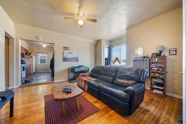 living area with light wood-style flooring, a ceiling fan, and baseboards