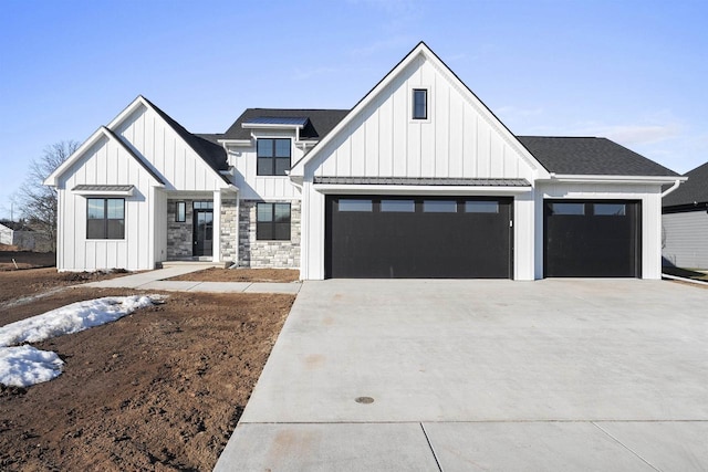 modern farmhouse featuring concrete driveway, stone siding, board and batten siding, and roof with shingles