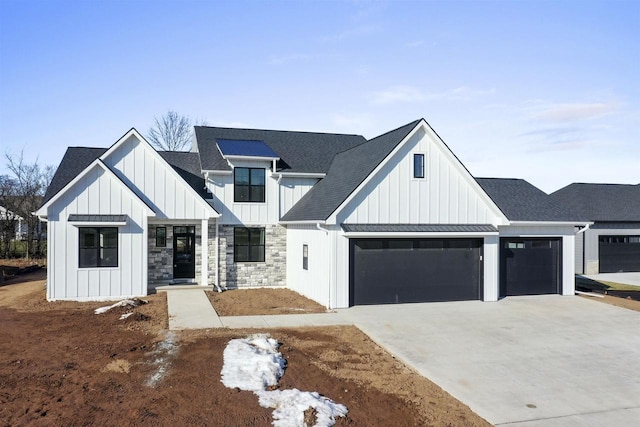 modern inspired farmhouse with a standing seam roof, stone siding, roof with shingles, board and batten siding, and concrete driveway