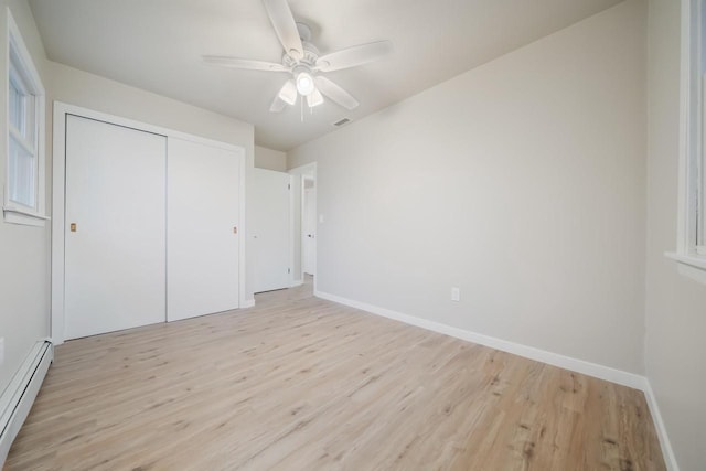 unfurnished bedroom featuring light wood-style floors, a closet, baseboards, and baseboard heating