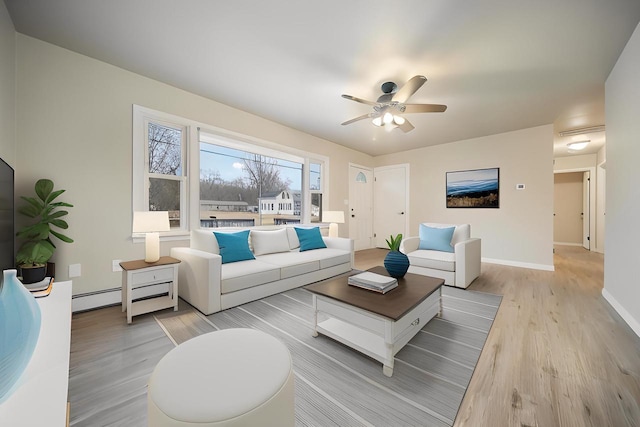 living area featuring light wood-style flooring, a ceiling fan, a baseboard heating unit, and baseboards