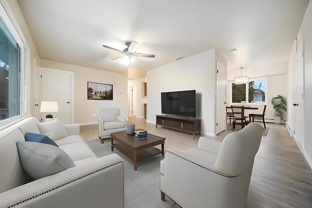 living room featuring baseboards, baseboard heating, light wood-style flooring, and a ceiling fan