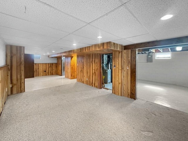 basement featuring a drop ceiling, heating unit, wood walls, concrete block wall, and carpet flooring