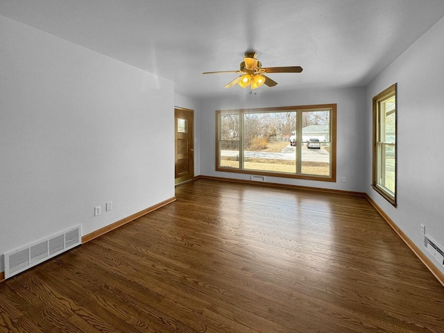 empty room featuring dark wood-type flooring, a ceiling fan, visible vents, and baseboards