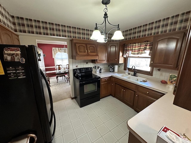 kitchen featuring black appliances, a sink, wallpapered walls, light countertops, and a chandelier