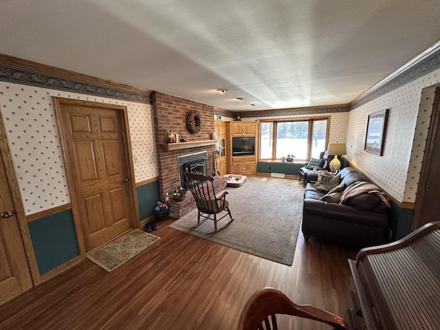 living room with a brick fireplace, wallpapered walls, dark wood finished floors, a wainscoted wall, and ornamental molding