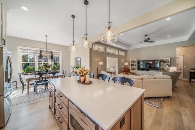 kitchen with light wood finished floors, recessed lighting, hanging light fixtures, appliances with stainless steel finishes, and ceiling fan with notable chandelier