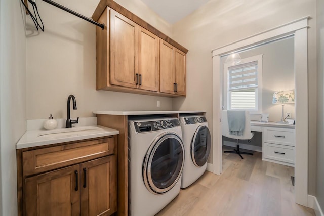 laundry room featuring cabinet space, washer and dryer, light wood-style flooring, and a sink