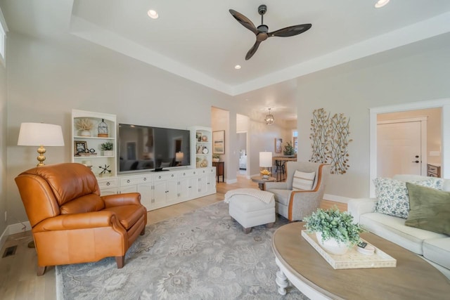 living area featuring light wood finished floors, baseboards, a tray ceiling, recessed lighting, and a ceiling fan