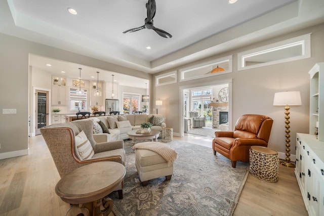 living room featuring a ceiling fan, recessed lighting, a stone fireplace, light wood finished floors, and baseboards