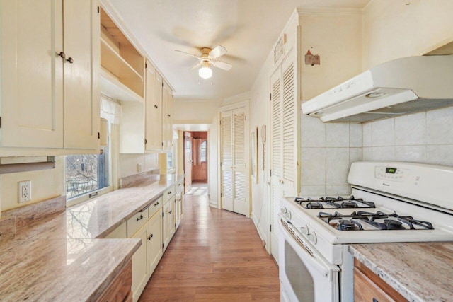 kitchen with under cabinet range hood, gas range gas stove, backsplash, light wood-style floors, and ceiling fan