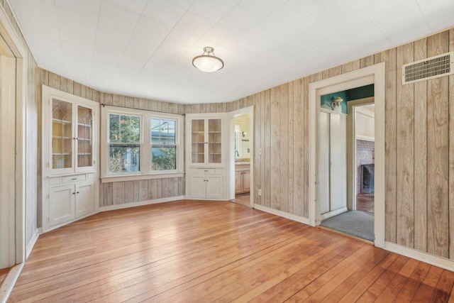 unfurnished room with light wood-style flooring, wooden walls, baseboards, and visible vents