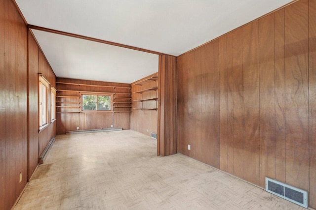 unfurnished room with visible vents, wood walls, and a baseboard radiator