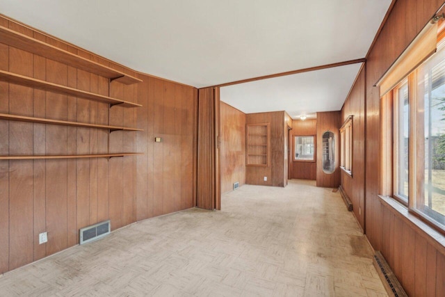 empty room with a baseboard heating unit, visible vents, and wood walls