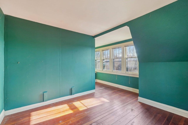 unfurnished room with hardwood / wood-style floors, lofted ceiling, and baseboards