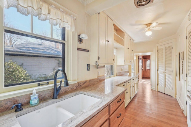 kitchen with visible vents, ceiling fan, light stone countertops, light wood-type flooring, and a sink