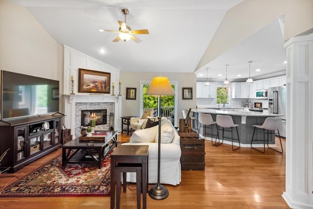 living area with light wood-style flooring, a fireplace, ceiling fan, and vaulted ceiling