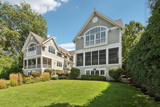 back of property with a lawn, stone siding, a sunroom, and a shingled roof