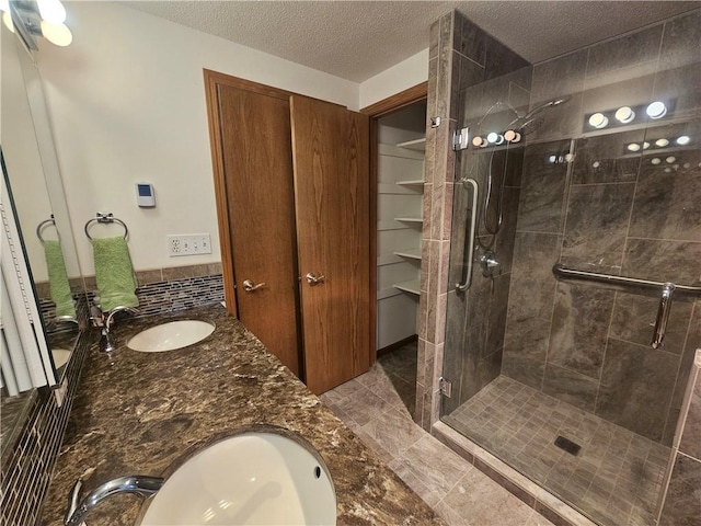 bathroom featuring double vanity, a shower stall, a textured ceiling, and a sink