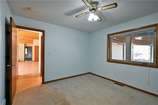 empty room featuring a ceiling fan, baseboards, visible vents, a textured ceiling, and light carpet