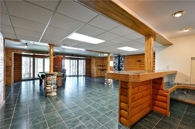 interior space with wooden walls, a paneled ceiling, indoor bar, and a sink