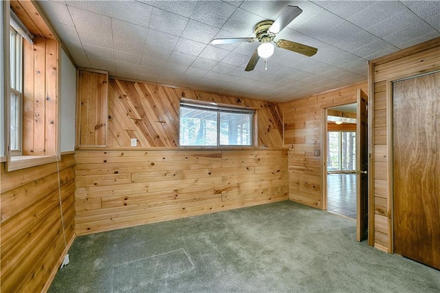 spare room with a ceiling fan, carpet, a healthy amount of sunlight, and wooden walls