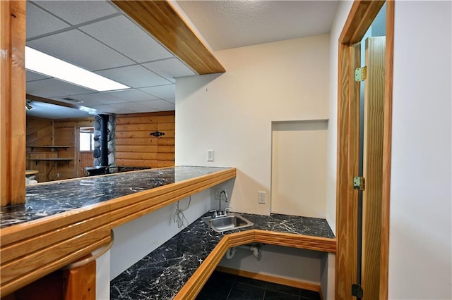 kitchen featuring a sink, a drop ceiling, wood walls, and tile countertops