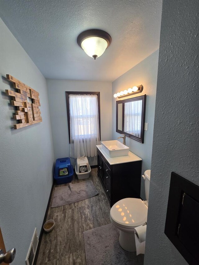 half bathroom with visible vents, toilet, vanity, wood finished floors, and a textured ceiling