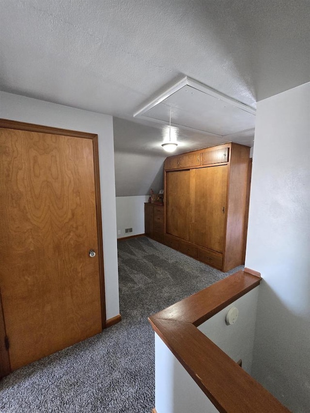 bonus room featuring visible vents, attic access, vaulted ceiling, a textured ceiling, and dark colored carpet