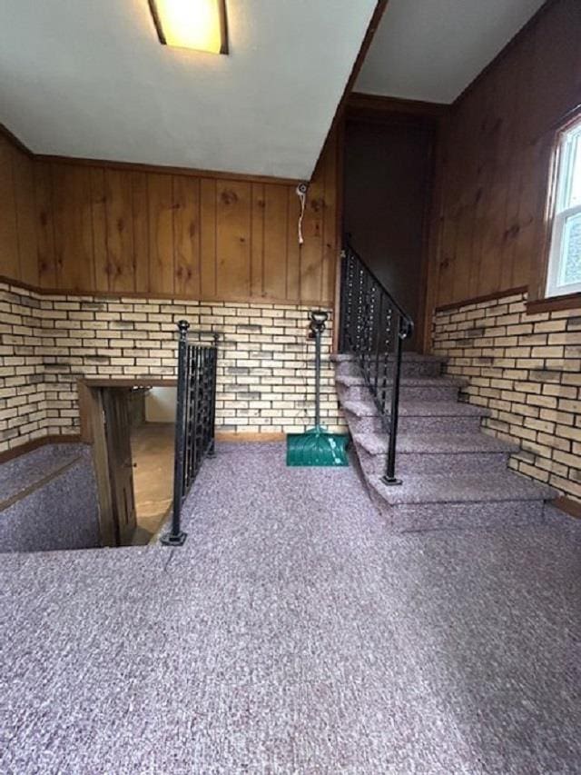 staircase featuring wood walls, brick wall, and carpet floors