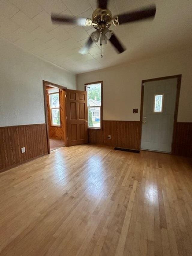 interior space with ceiling fan, wooden walls, light wood-style floors, and wainscoting