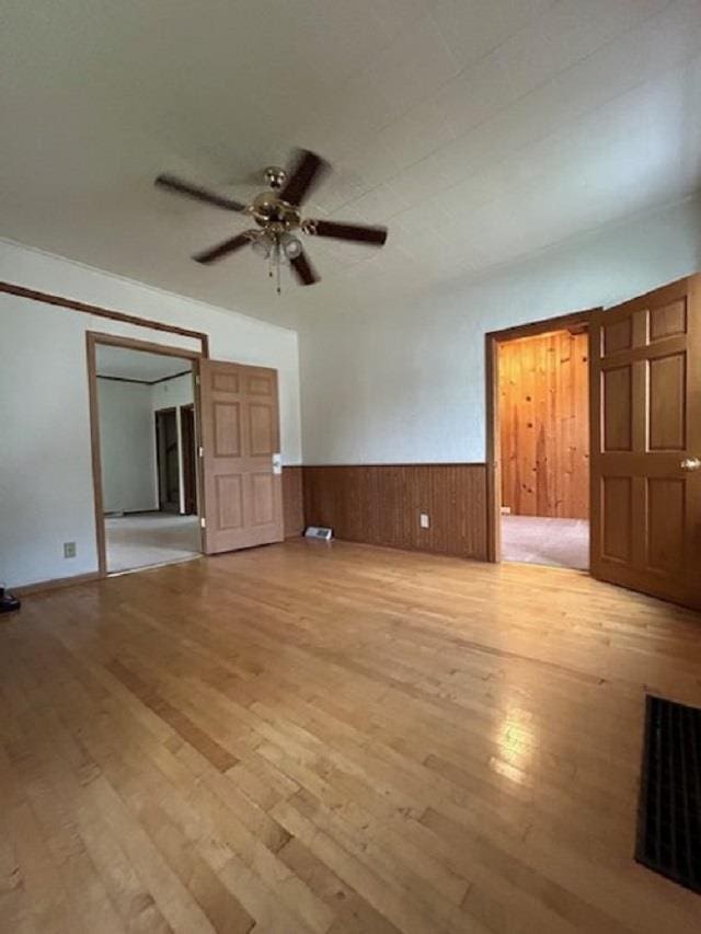 unfurnished living room featuring light wood-style flooring, a wainscoted wall, wooden walls, and ceiling fan