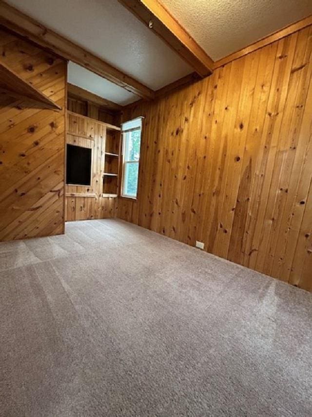 unfurnished living room with beam ceiling, carpet flooring, wood walls, and a textured ceiling