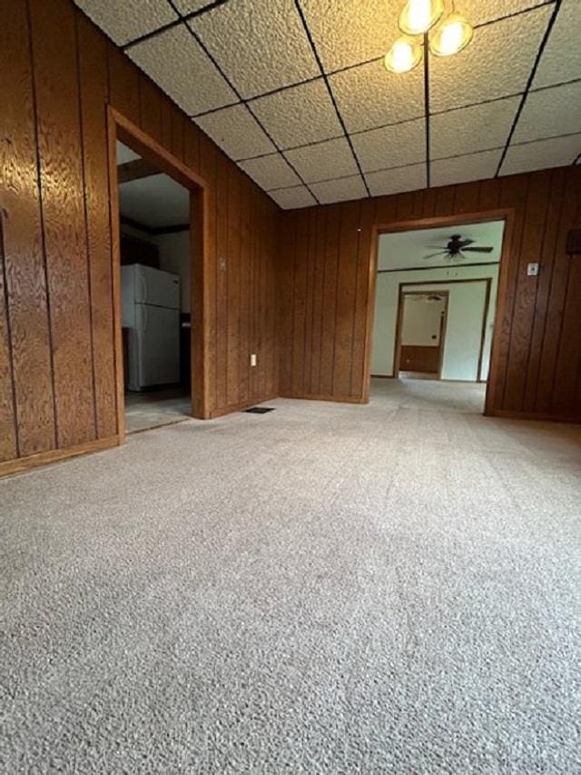 empty room with light carpet, wooden walls, and a drop ceiling