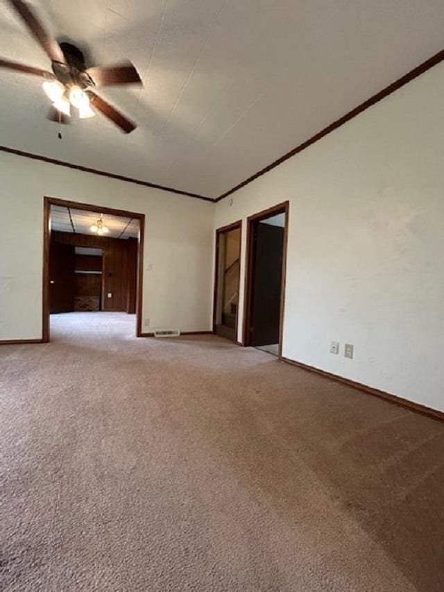 unfurnished room featuring a ceiling fan, crown molding, light colored carpet, and baseboards