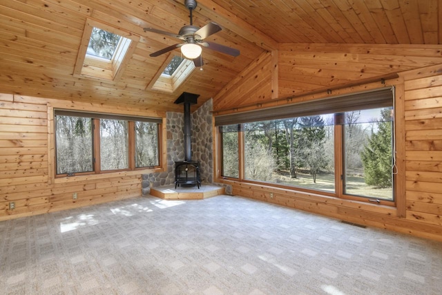 unfurnished living room featuring wooden walls, carpet, wooden ceiling, a wood stove, and a ceiling fan