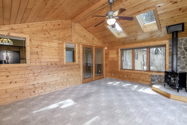 unfurnished living room with wooden walls, vaulted ceiling with skylight, a wood stove, ceiling fan, and wood ceiling