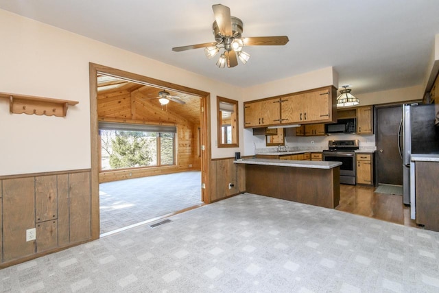 kitchen with a peninsula, wooden walls, wainscoting, and stainless steel appliances