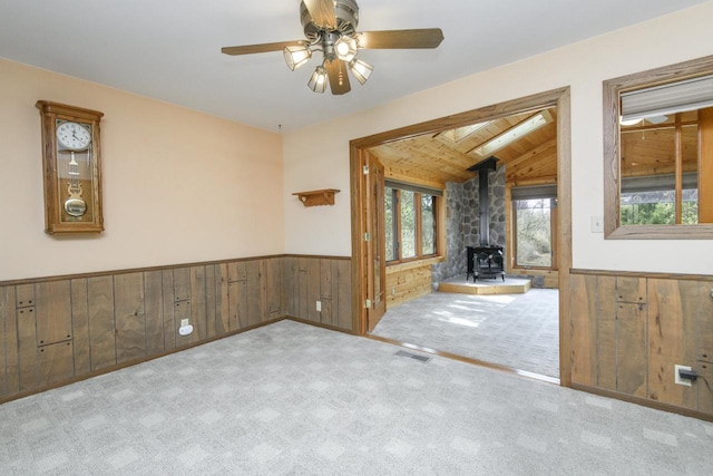 unfurnished living room featuring a wood stove, wooden walls, and wainscoting