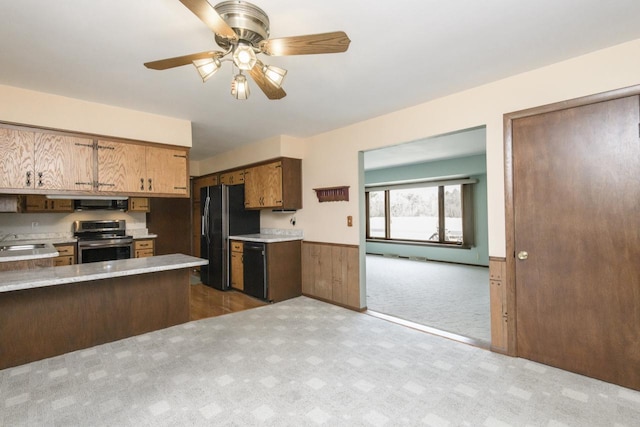 kitchen with a sink, stainless steel range with electric cooktop, light countertops, wainscoting, and black refrigerator with ice dispenser