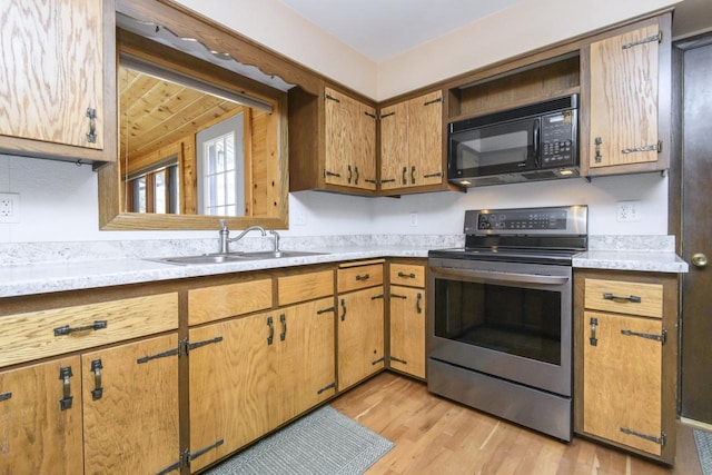 kitchen featuring black microwave, light countertops, light wood-type flooring, electric stove, and a sink