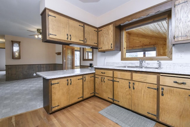 kitchen featuring a wainscoted wall, a sink, a peninsula, light countertops, and ceiling fan