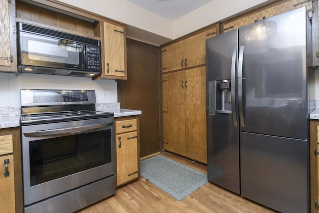 kitchen featuring brown cabinets, appliances with stainless steel finishes, light wood-style flooring, and light countertops