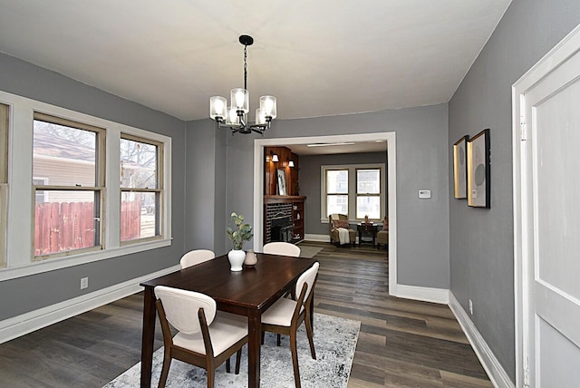 dining space featuring baseboards, a fireplace, a chandelier, and dark wood-style flooring