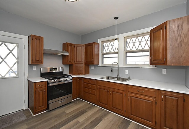 kitchen featuring stainless steel range with gas cooktop, under cabinet range hood, dark wood finished floors, brown cabinets, and a sink