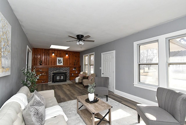 living room with a glass covered fireplace, wooden walls, wood finished floors, and ceiling fan