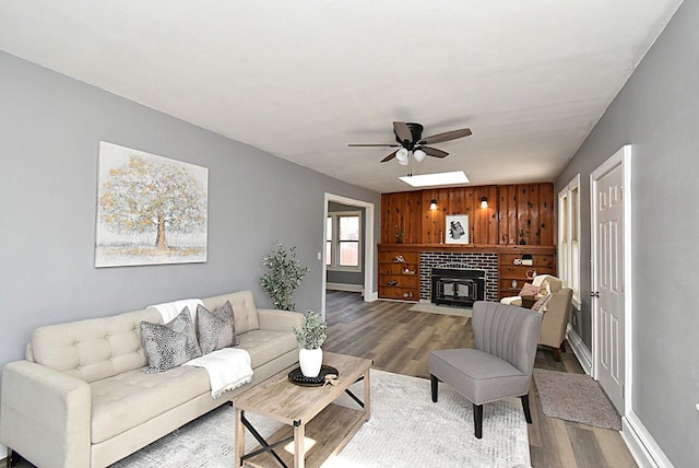 living area with baseboards, wood finished floors, ceiling fan, and a fireplace with flush hearth